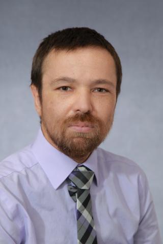White male with short brown hair and beard, wearing light shirt and patterned tie